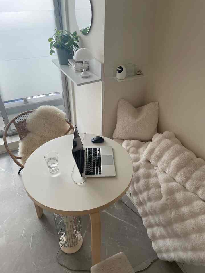 White and wood tone compact studio apartment featuring round table, cozy bed, and natural ambiance