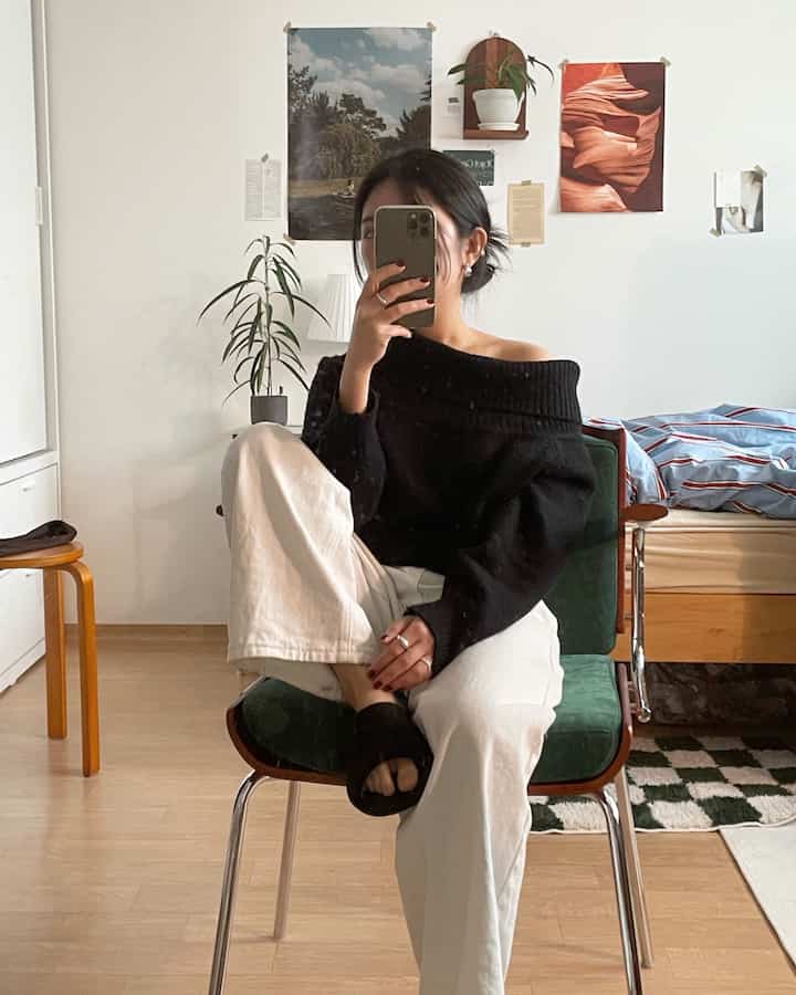 Natural bedroom with white walls and wood-tone floor, featuring a stool and plants for a mirror selfie setup