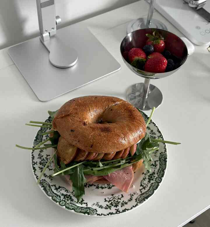 Clean kitchen setting with white table surface featuring brown bagel sandwich and stainless dessert bowl