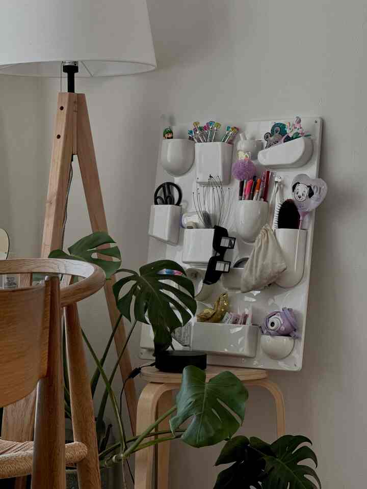 ナチュラルトーンの木製スツールと白い壁掛け収納、大きな葉の植物が置かれた居心地の良いリビングコーナー