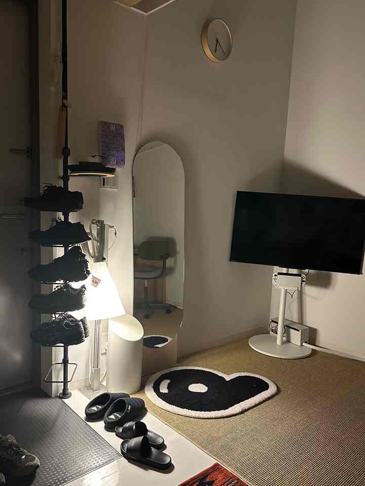 白と黒のモノトーンカラーの狭いワンルーム玄関、靴の収納がされたテンションロッドとスタンドミラーが配置された清潔感のある空間