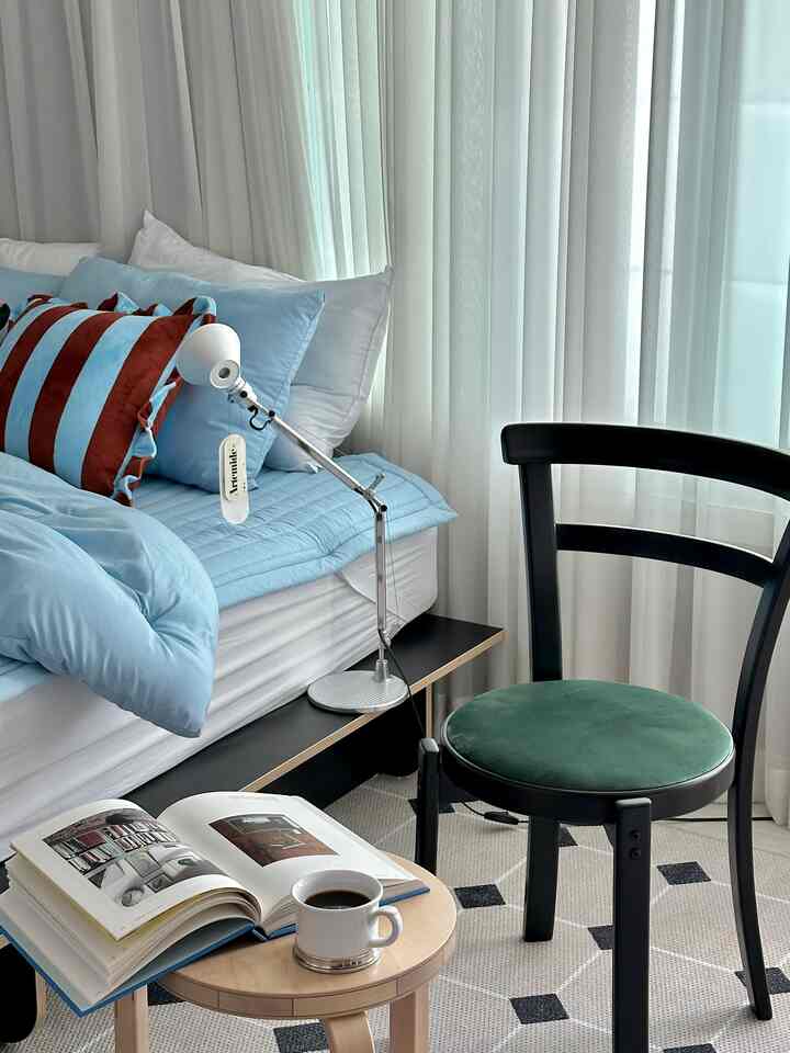 Bright and calm bedroom by the window featuring blue bedding and a black chair