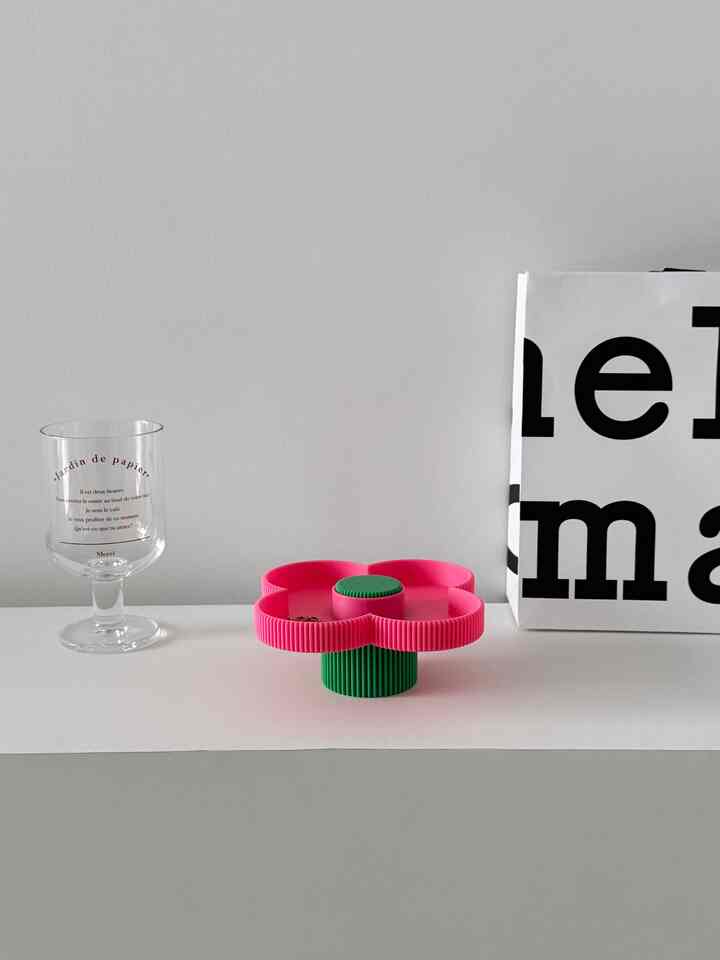 ホワイトの背景にピンクの花形トレイと緑の台座が置かれたシンプルなインテリア小物の写真