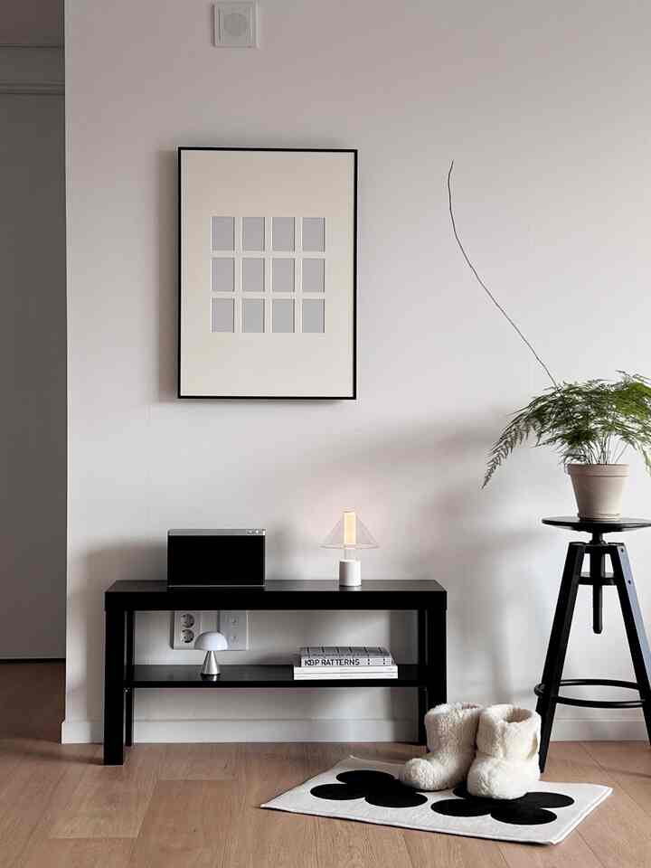 白い壁と木目調の床のリビング、黒い棚にランプと額縁が配置された雰囲気のあるインテリア