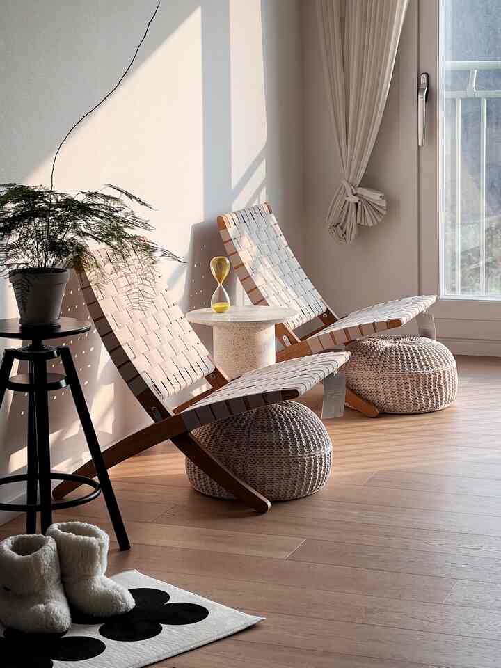 ナチュラルなベージュトーンのリビング、木製フレームの椅子とニットポフ、サイドテーブルが配置された雰囲気のあるインテリア