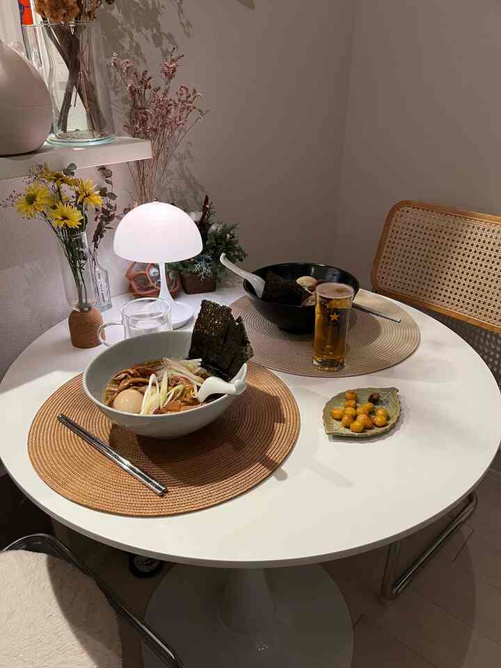 白とベージュの北欧風ダイニングルーム、丸テーブルにラーメンとビールが配置されたシンプルで落ち着いた雰囲気の空間