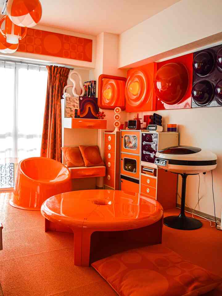 鮮やかなオレンジ色調のリビング、丸いプラスチックのテーブルと椅子が配置されたレトロで個性的な空間