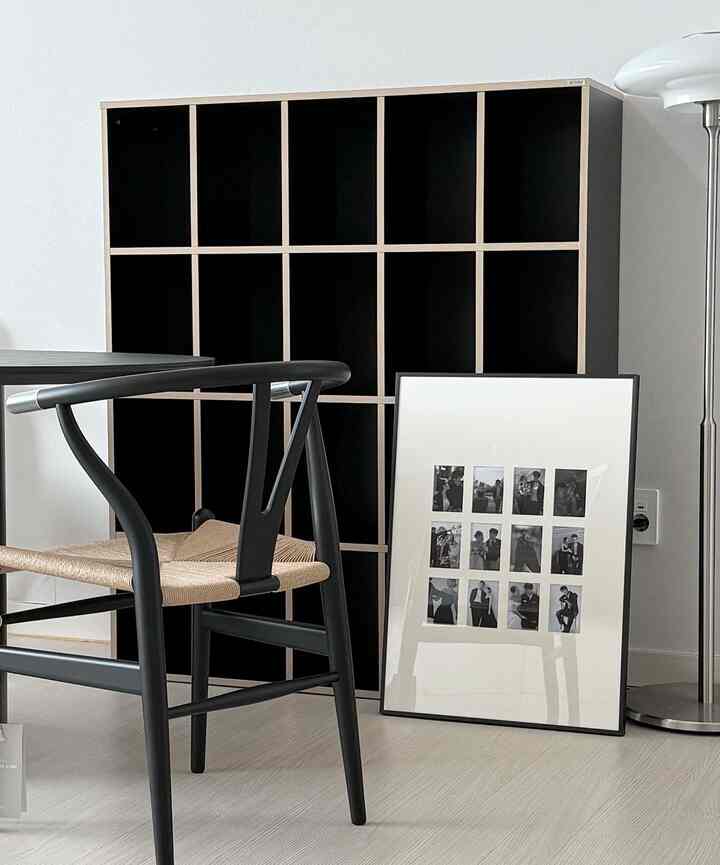 黒と白のトーンのリビング、CARL HANSEN & SONウィッシュボーンチェアと黒い本棚、モノクロのウェディング写真フレームが配置されたシンプルでモダンなインテリア