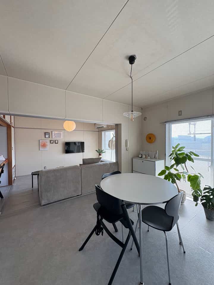 明るくナチュラルな色調の3DKリビング兼ダイニングスペース、白い円形ダイニングテーブルと黒い椅子、自然光と植物が配置された雰囲気のあるインテリア