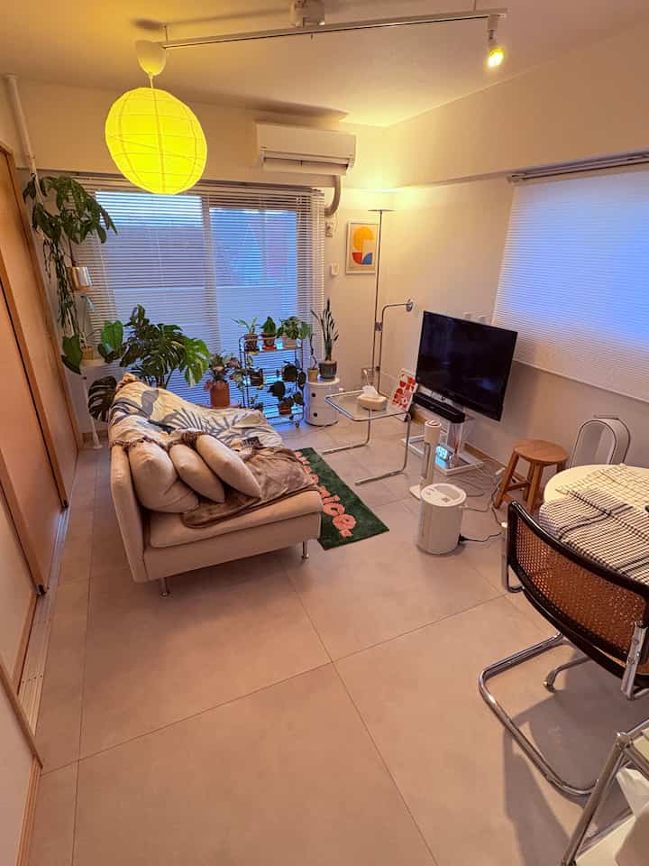 白い壁と木目調の引き戸がある狭いリビング、黄色いペンダントライトと植物がアクセントの雰囲気ある空間