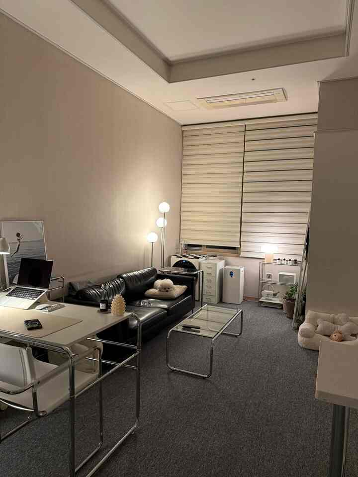 グレーのタイルカーペットと黒いレザーソファが配置されたワンルームのミッドセンチュリーモダンで居心地の良い空間