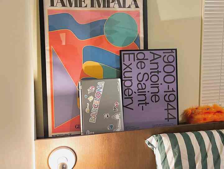 Warm bedroom home office with white walls, brown wooden desk, laptop, and artistic posters on the wall