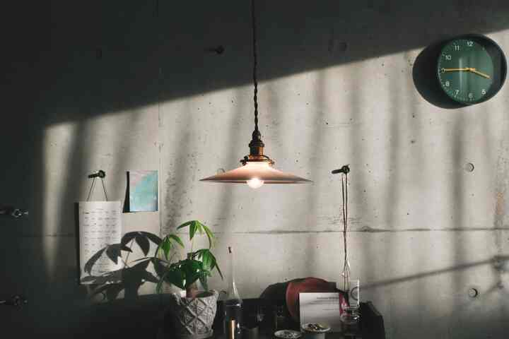 ナチュラルなグリーントーンのリビング、中央にペンダントライトと壁時計、観葉植物が配置された落ち着いたモダンな雰囲気のインテリア