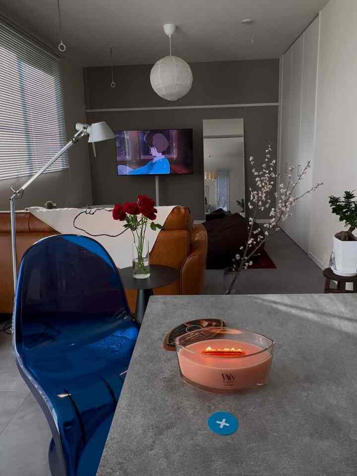 グレーのコンクリートテーブルと透明な青い椅子があるモダンでナチュラルなリビング、ブラウンのソファとアロマキャンドルが配置された雰囲気のあるインテリア