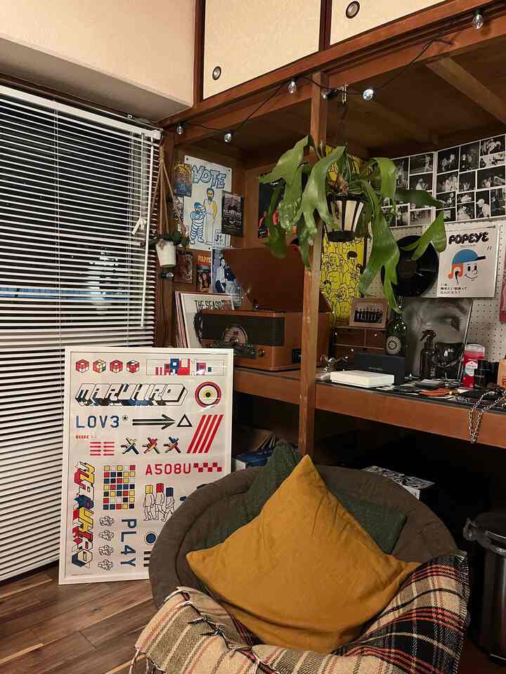Small cozy corner room with brown wood tones and vintage decor featuring a cushioned chair, vintage turntable, shelving, and a hanging plant