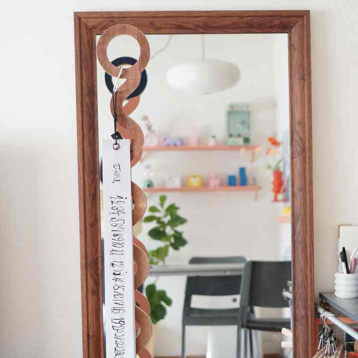 白い壁と茶色の木製フレームの鏡が配置されたシンプルな空間で、ダイニングチェアと植物が落ち着いた雰囲気を演出しています。