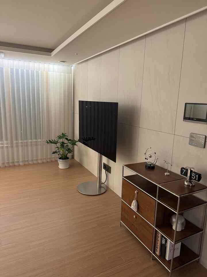 白い壁と木目調の床のモダンなリビング、テレビ台と収納が配置された清潔感のある空間