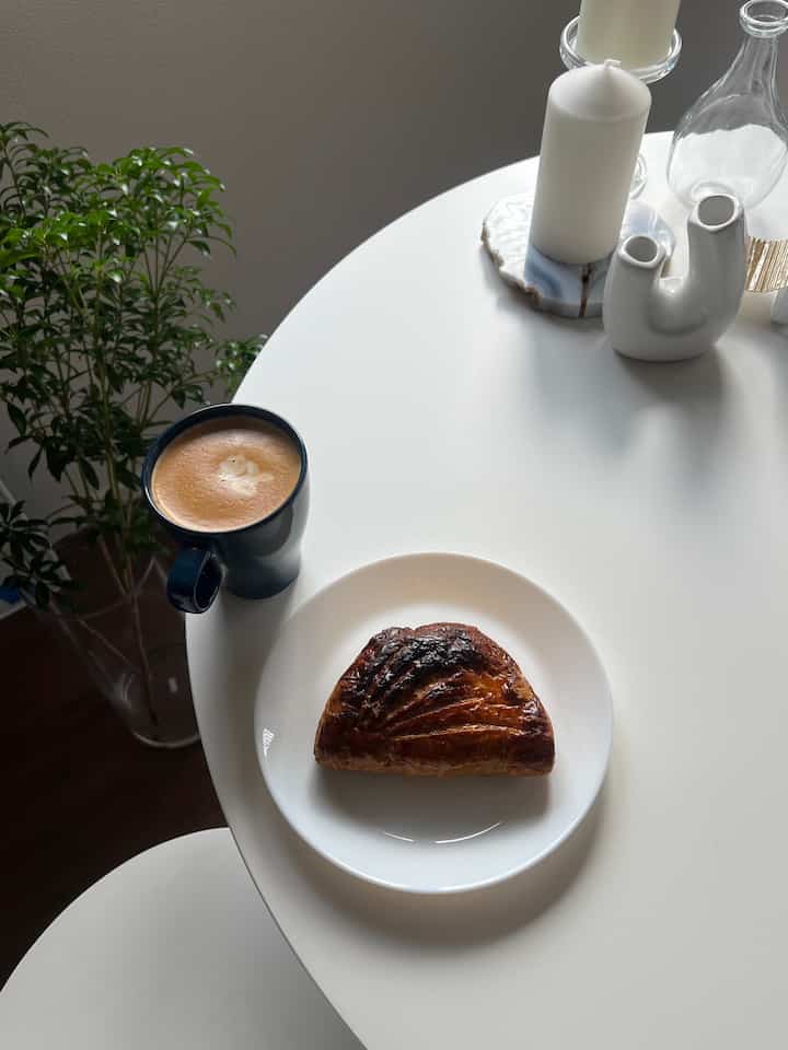 ナチュラルな色調のキッチンスペース、白い丸テーブルにキャンドル、マグカップ、焦げ目のあるアップルパイが置かれた雰囲気のあるおうちカフェ