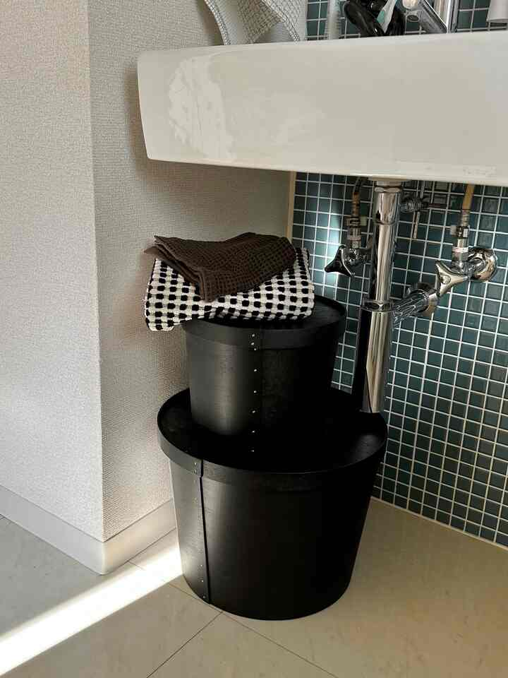 ブラックの収納ボックスと青いタイル壁が配置された浴室の洗面下スペース、清潔でモダンな雰囲気のインテリア