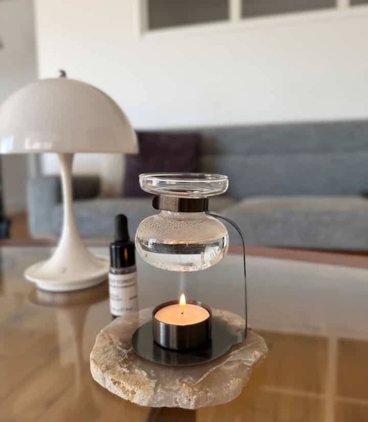 白と木目調の調和が美しいリビング、グレーのソファとアロマオイルウォーマー、テーブルランプが落ち着いた雰囲気を演出するインテリア