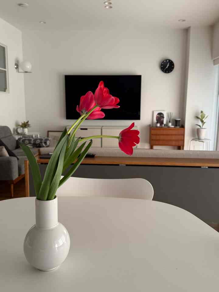 白と木目調が調和した北欧風リビングとダイニング、中央に赤いチューリップの花瓶を配した印象的な空間