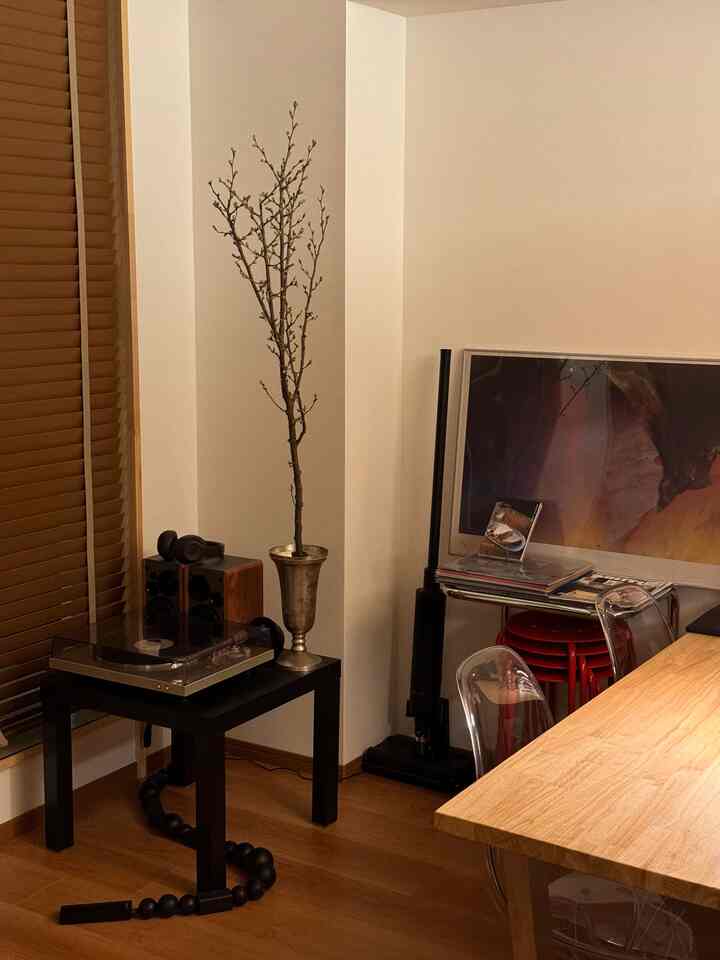 ブラウンの木目調床と白い壁が調和する一人暮らしのリビング、レトロなオーディオシステムとサイドテーブルが配置された雰囲気のある空間