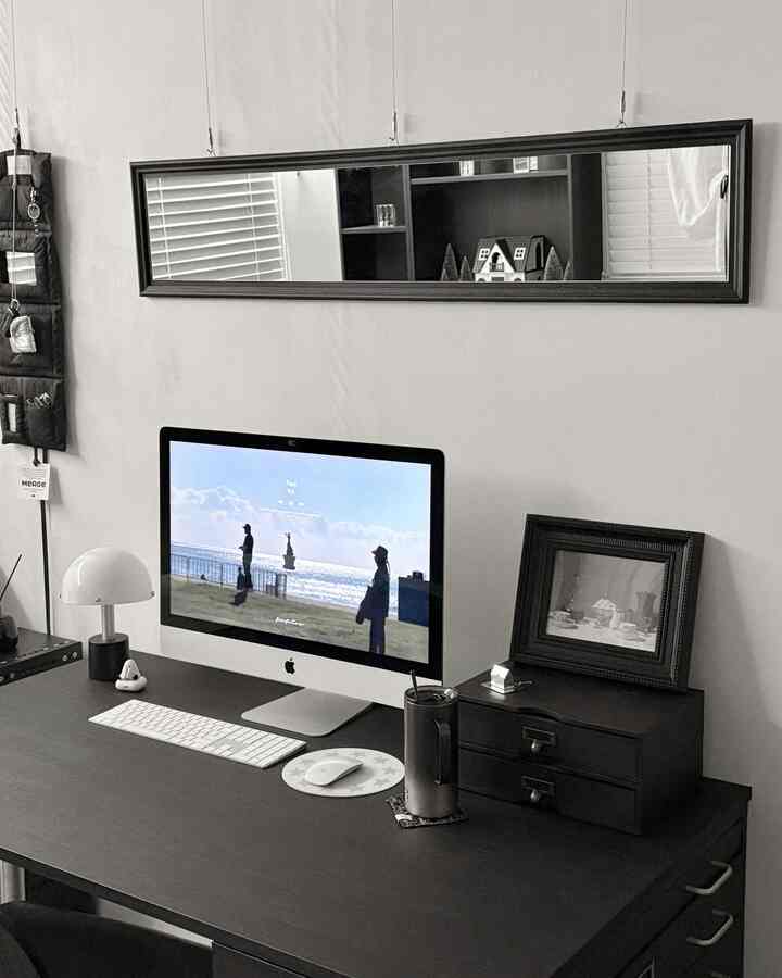 黒と白のトーンが特徴的なホームオフィス、広いデスクにコンピューターと壁掛け鏡、額縁が配置されたシンプルなインテリア