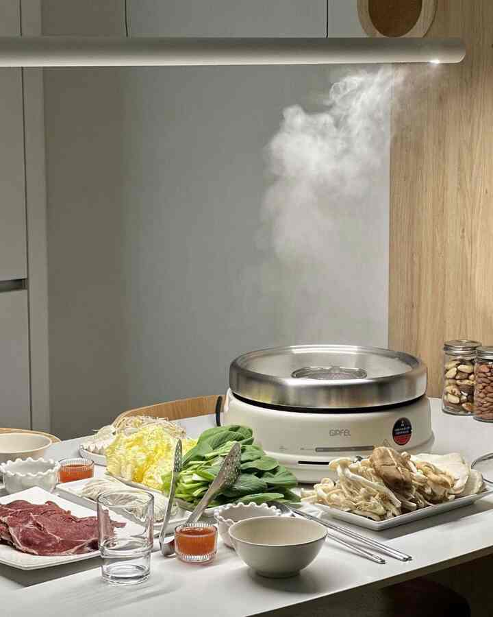 白とナチュラルの色調のキッチン、中央にしゃぶしゃぶ鍋と新鮮な野菜が並ぶ清潔感のあるホームクッキング空間