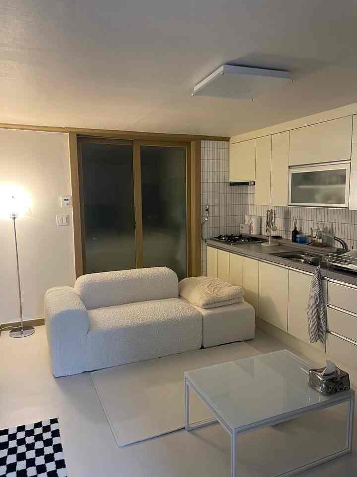 ホワイト調のコンパクトなキッチンとリビング、2人用ソファとシンプルな家具が配置された清潔感のある空間