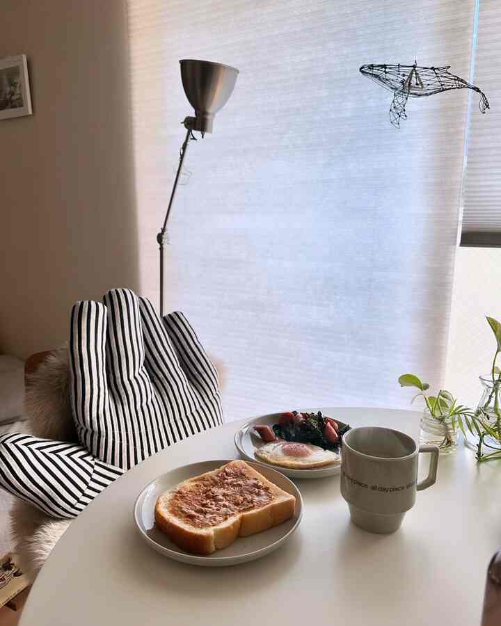 White-toned dining room featuring round table with simple breakfast and mug, creating a cozy and minimalist atmosphere