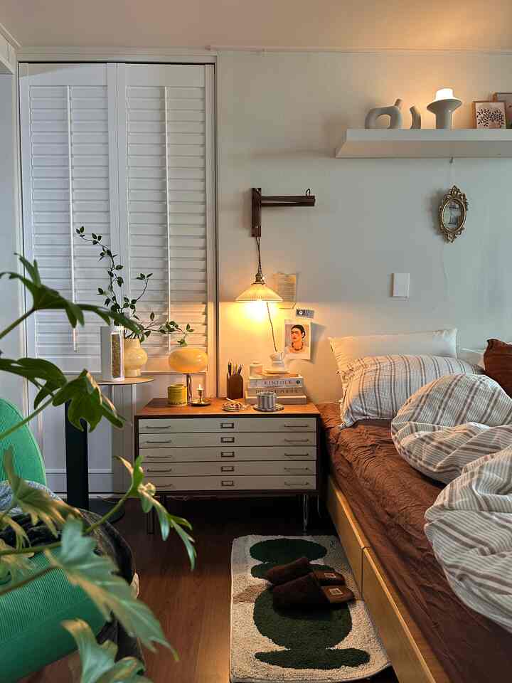 Cozy bedroom with warm wood tones and natural plants, featuring a nightstand and wall lighting creating a soothing atmosphere