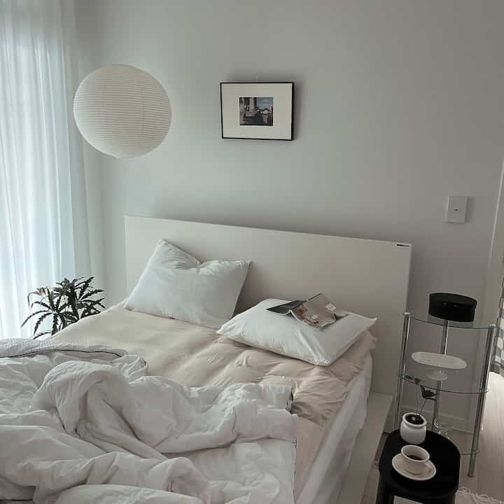 A white and beige tone bedroom featuring bed, stool, and nightstand with a simple and modern design