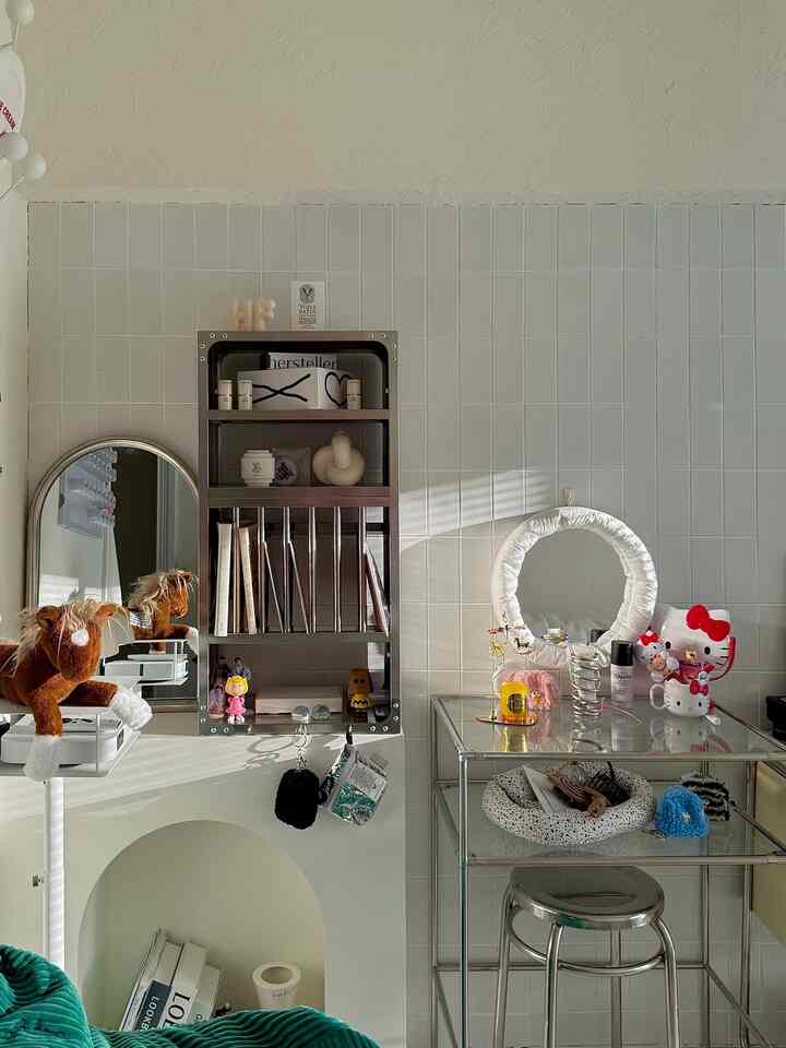Cozy space with white tiled wall, silver mirror, metal frame bookshelf, and glass table with decorative items