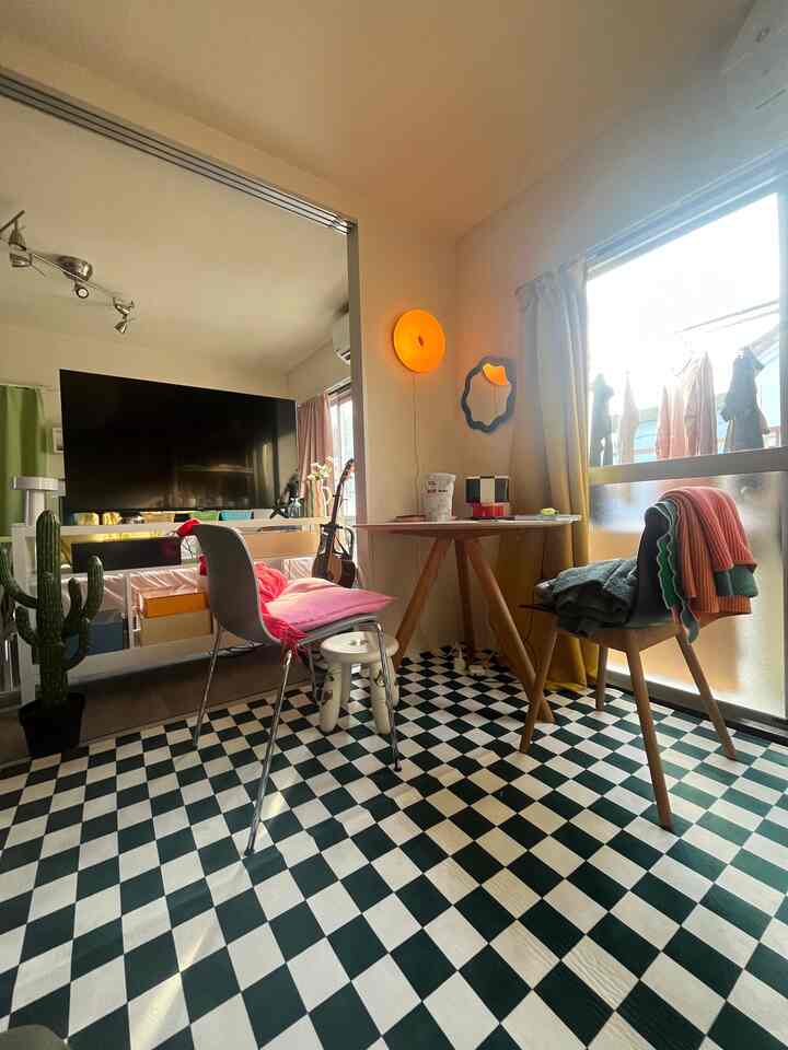 Living room featuring black and white checkered rug, wooden desk and chairs, and warm yellow wall lamp creating a cozy atmosphere