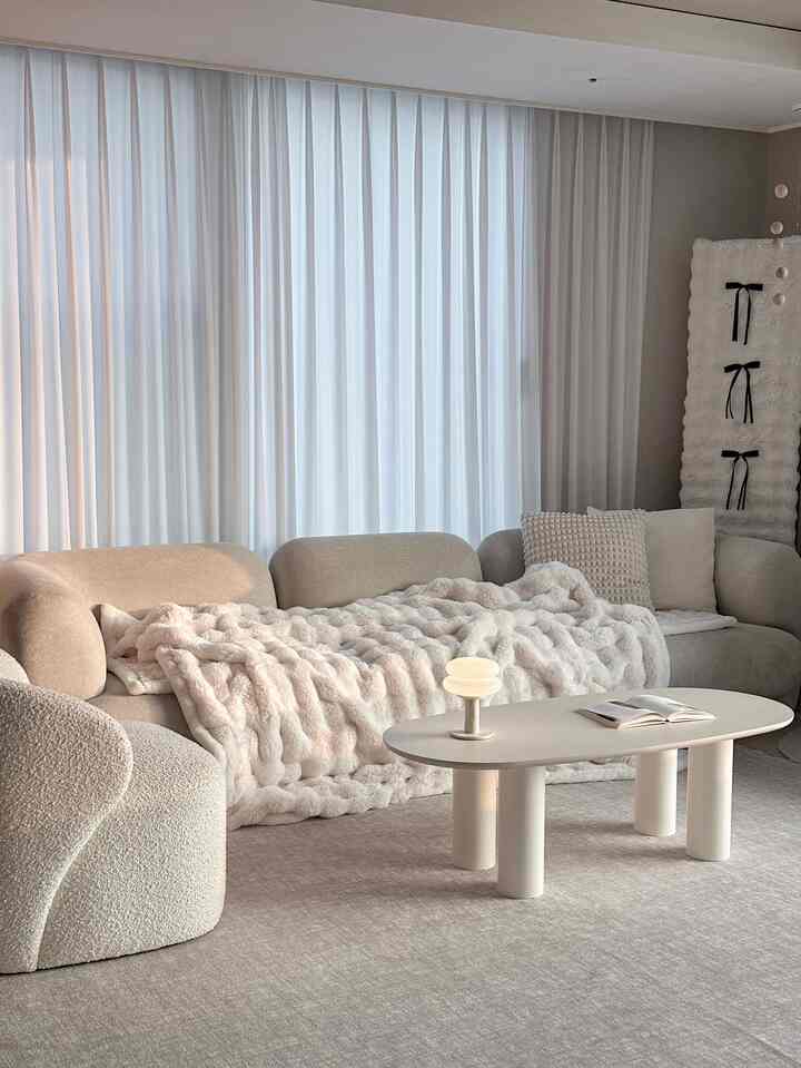 Beige and ivory toned living room featuring soft curved sofa and minimalist coffee table with cozy atmosphere