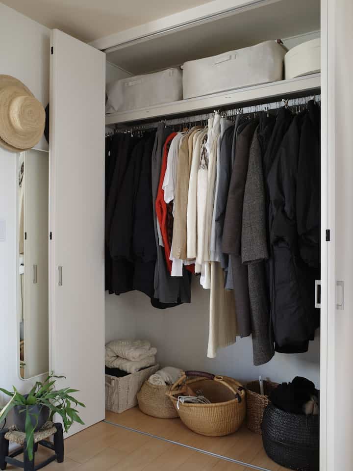 Natural style closet in white and brown tones featuring neatly arranged baskets and hanging clothes inside