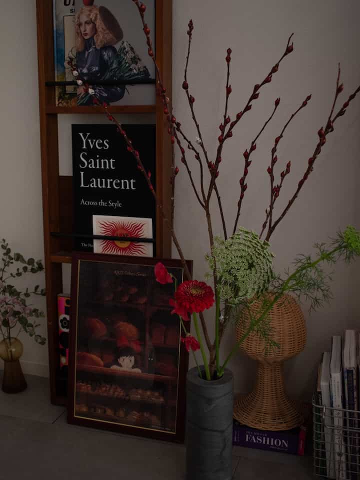 白色の壁と木製の棚、ラタンのアイテムと花瓶が配置されたナチュラルな雰囲気のワンルームの一角