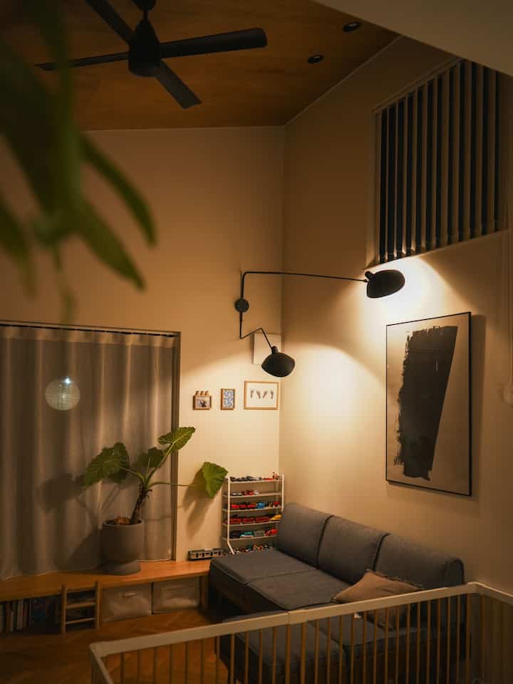 温かみのあるナチュラルカラーの勾配天井リビング、ネイビーソファと観葉植物、ブラケットライトが配置された雰囲気のある空間