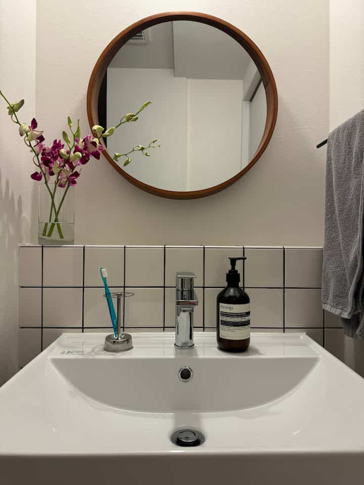 白と木目調のモダンな洗面スペース、丸い鏡と洗面台上の用具が配置された印象的な空間
