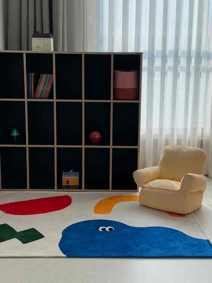 White and navy toned kids' room featuring a large bookshelf, yellow checkered kid armchair, and colorful rug with a warm atmosphere