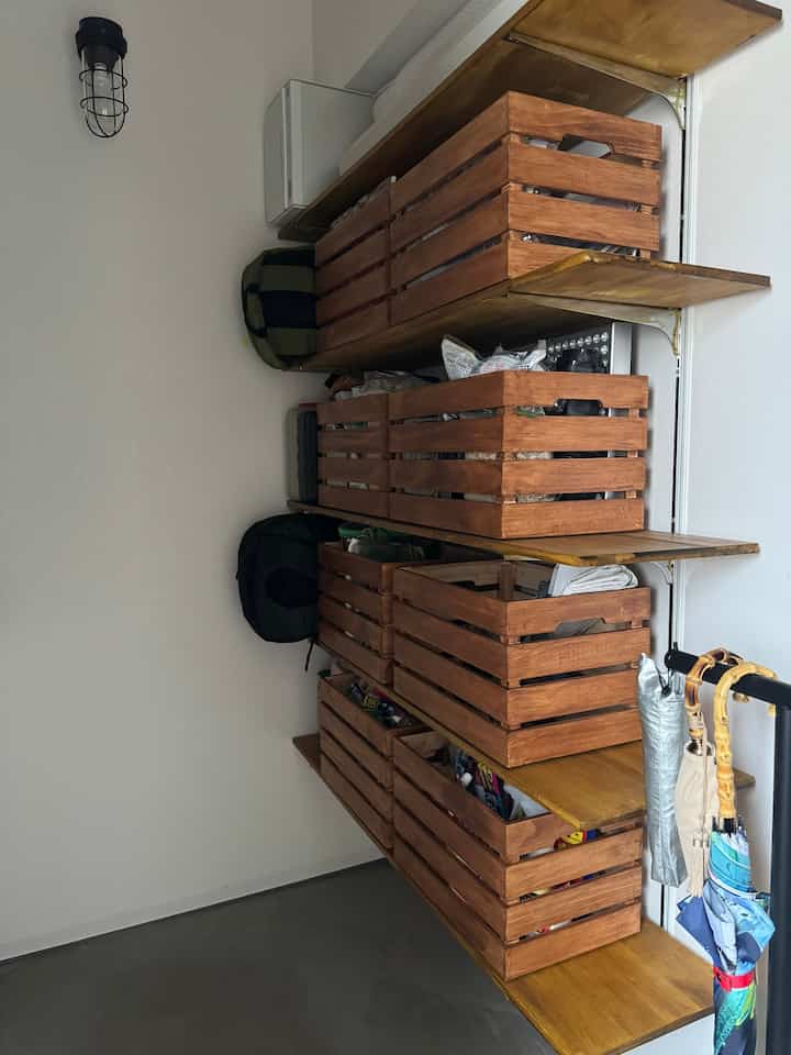 白い壁と木目調の棚が配置された玄関、傘立てと整頓された収納バスケットが印象的な空間