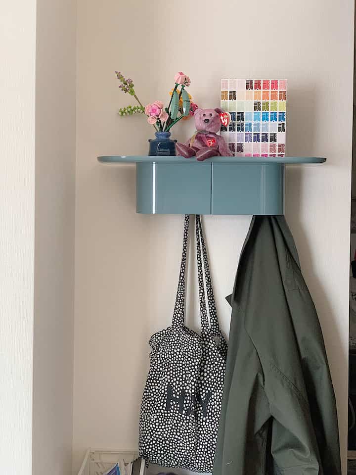 An entrance storage space featuring a pastel blue wall-mounted shelf with decorative items against a beige wall background