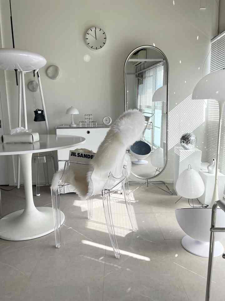A white and natural-tone studio living room featuring a transparent armchair, large floor mirror, and floor lamps in a modern style