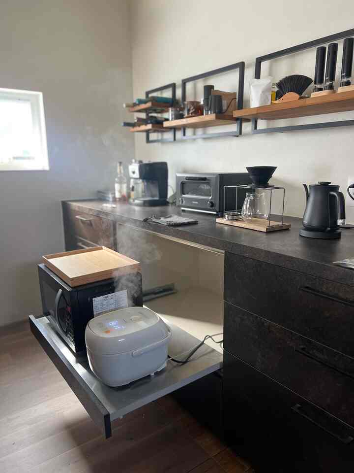 モダンな黒と白のキッチン、壁棚と電子レンジ、電気ケトルが配置された機能的な空間