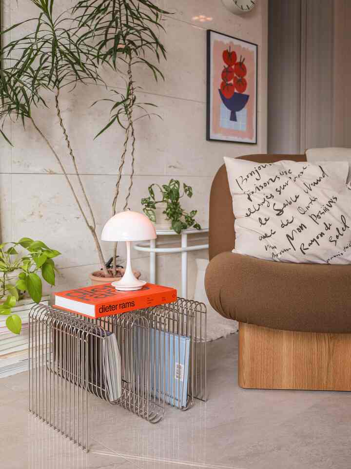 ナチュラルなブラウンとホワイトの色調のリビング、木製ソファとワイヤーシェルフ、テーブルランプ、植物が調和した雰囲気あるインテリア