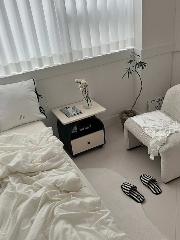 A natural modern bedroom in soft beige and white tones featuring a simple armchair and nightstand