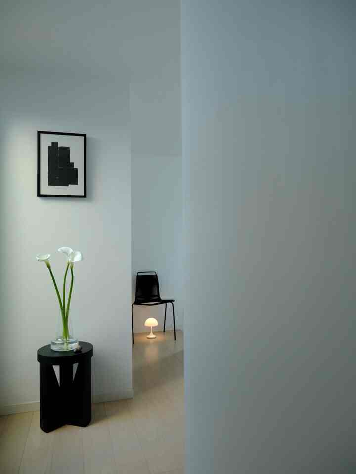 白と黒の色調の玄関または小さなリビング、花瓶とフロアランプが配置されたミニマルな空間