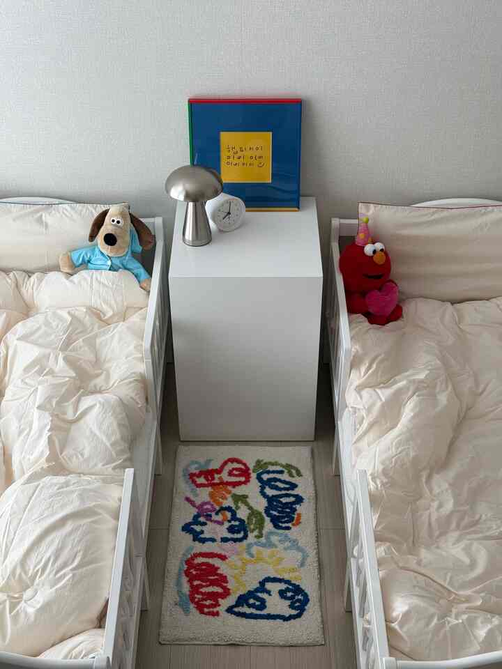 白とナチュラルカラーの子供部屋、二つのベッドとカラフルなラグが配置されたシンプルな兄妹共有の部屋のインテリア