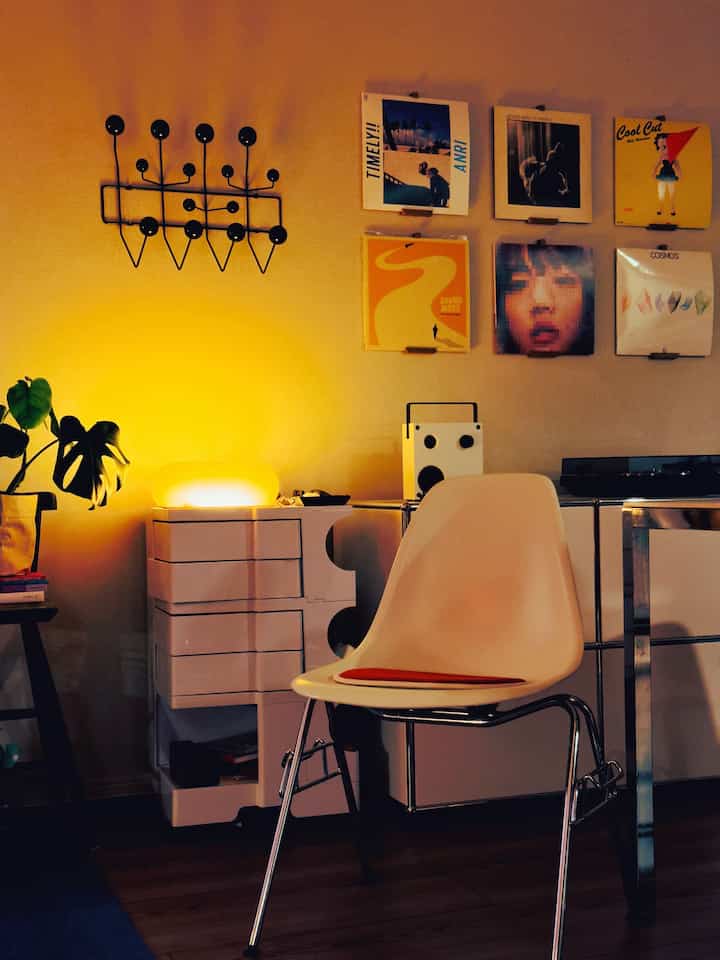 暖かい黄色の照明が照らすリビング、白いアームチェアとサイドテーブル、壁にはヴィンテージなインテリア小物が配置された雰囲気のある空間