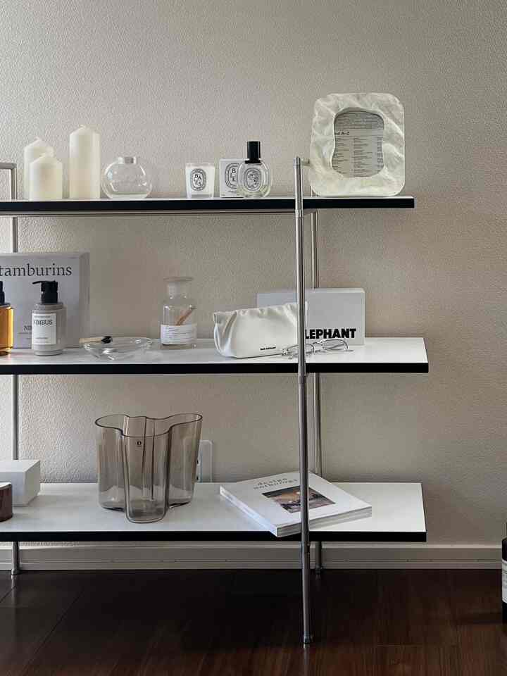 ベージュの壁と白い棚が配置されたナチュラルなトーンのリビング、キャンドルとガラスの装飾品が整然と並ぶ印象的なインテリア